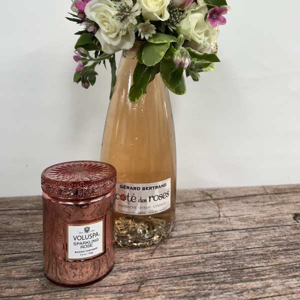 Pink and white rose bouquet in a glass bottle with a rose candle in front