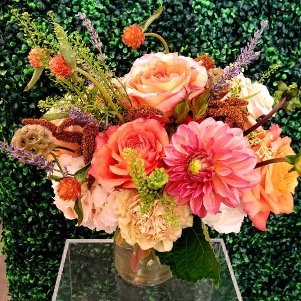 Mixed bouquet of peach, pink, and cream flowers in a clear glass vase