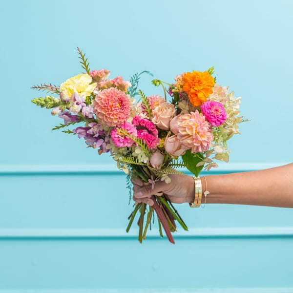 Handheld bouquet of pink, peach, yellow, and orange flowers