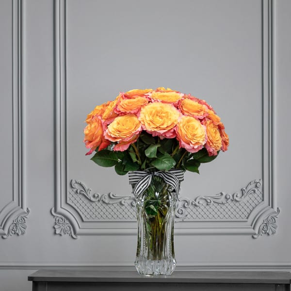 Orange and pink roses arranged in a clear glass vase with a striped ribbon