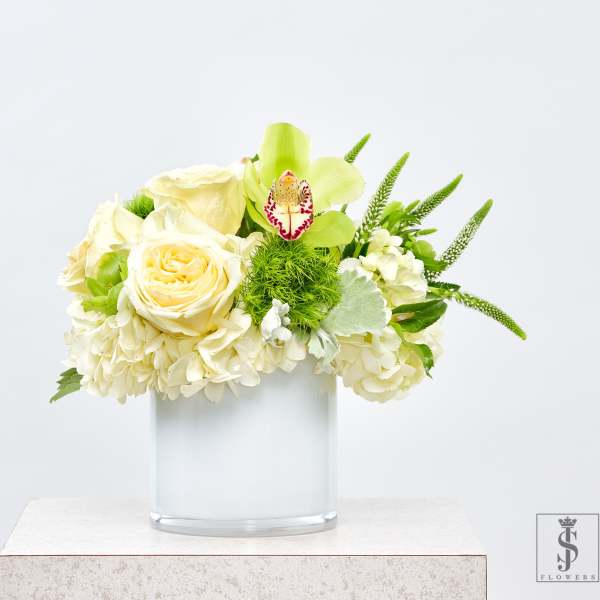 Cream roses and hydrangeas in a clear glass vase with green accents