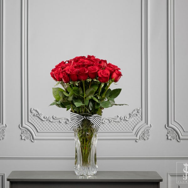 Red roses in a clear glass vase with a striped ribbon
