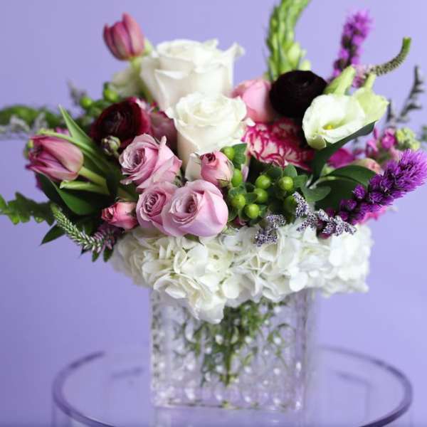 Mixed bouquet of roses, hydrangeas, and purple blooms in a clear vase