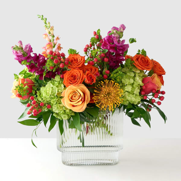 Colorful bouquet of roses, hydrangeas, and snapdragons in a clear glass vase