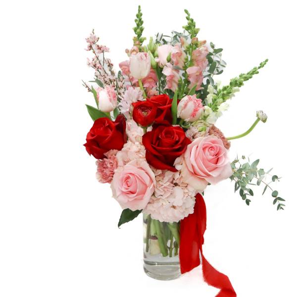 Red and pink roses in a clear glass vase with a red ribbon