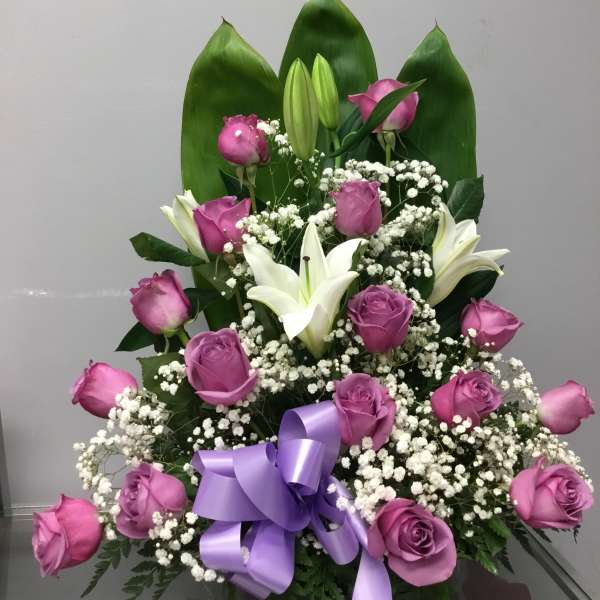 Pink roses and white lilies arranged with baby's breath and a purple ribbon