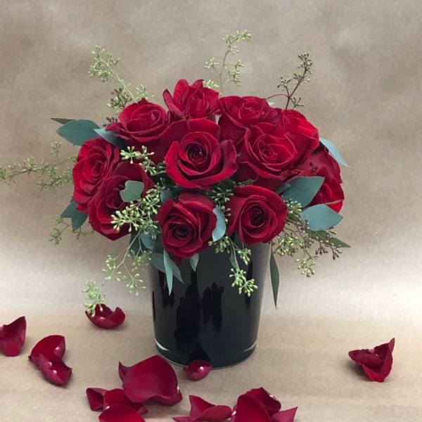 Red rose bouquet in a black vase with scattered petals