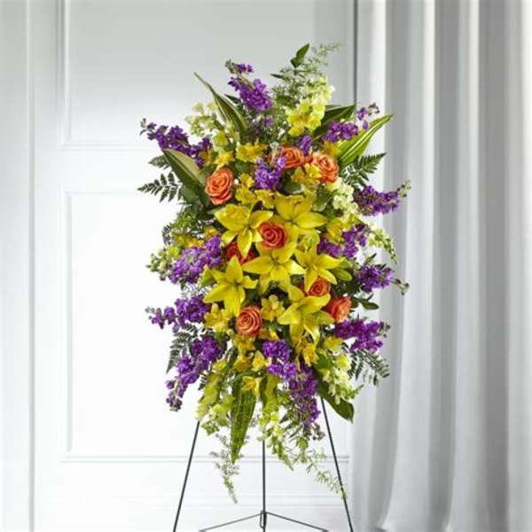 Tall standing floral spray with yellow lilies, orange roses, and purple flowers