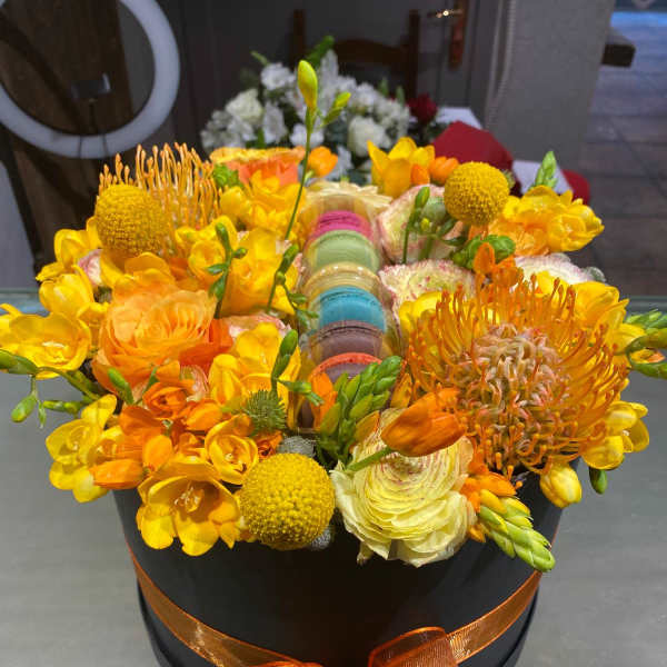 Orange and yellow floral arrangement in a black hatbox with ribbon