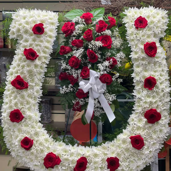 Heart-shaped white floral wreath with red roses and a white ribbon bow
