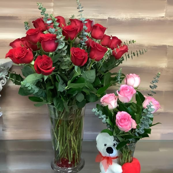 Two rose bouquets in glass vases, one with a teddy bear and heart