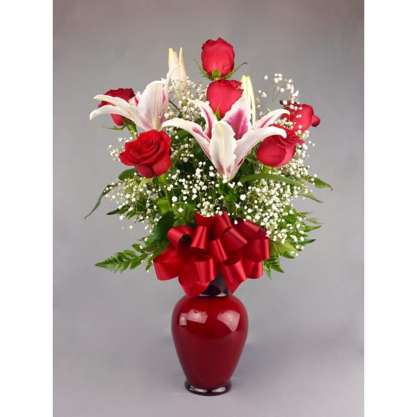 Red roses and white lilies in a red vase with a ribbon bow