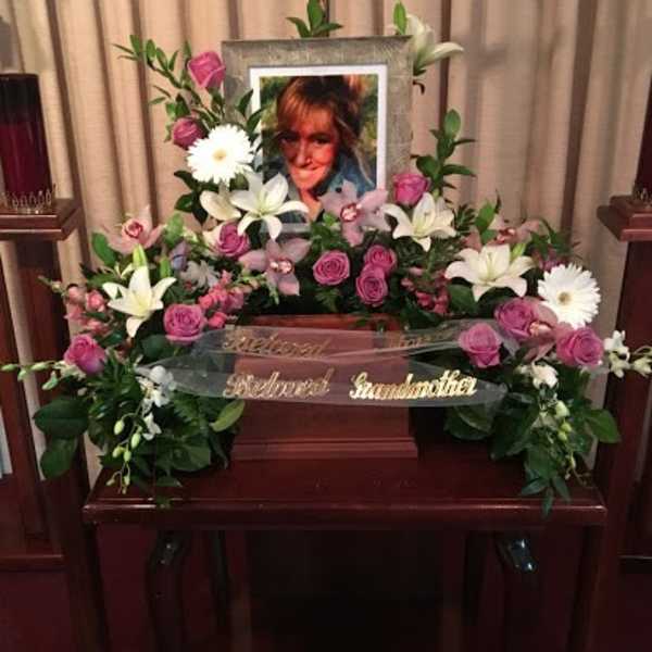 Floral funeral tribute with pink roses, white lilies, and daisies around a framed photo