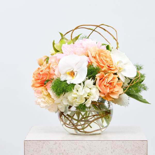 Peach roses and white orchids in a glass vase