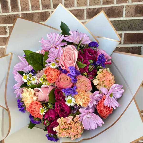 Mixed bouquet of pink, purple, and peach flowers wrapped in white paper