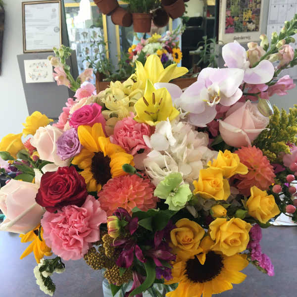 Mixed bouquet of roses, lilies, orchids, and sunflowers in a glass vase