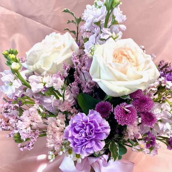 Bouquet of white roses and purple flowers in a vase with a pink ribbon