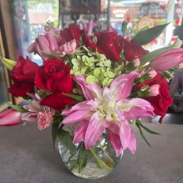 Round glass vase arrangement with red roses, pink lilies, tulips, and green hydrangea