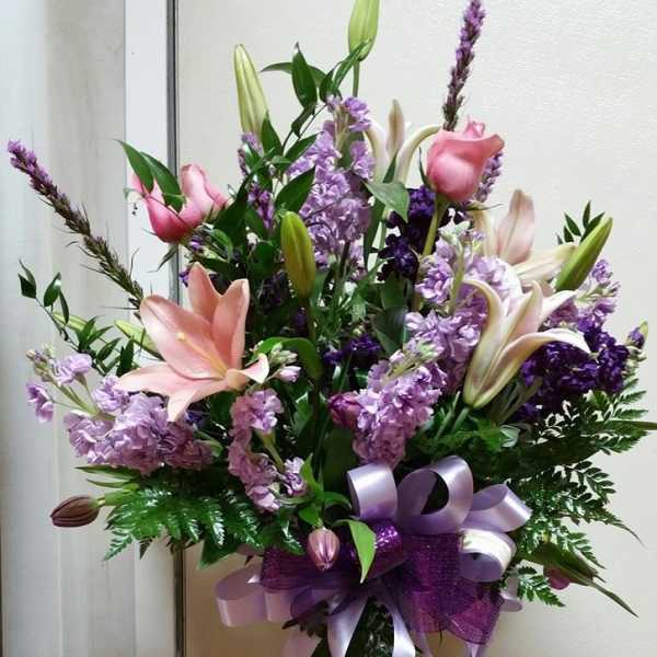 Pink lilies and purple flowers in a glass vase with a lavender ribbon