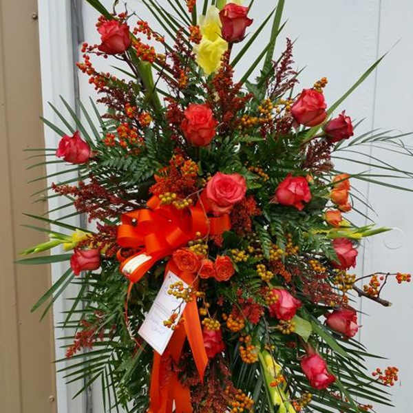 Tall standing floral spray with red roses and orange berries on an easel