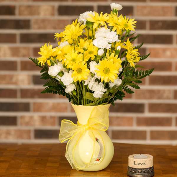 Yellow and white daisy bouquet in a pale vase with a ribbon