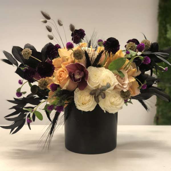 Peach, cream, and burgundy flower arrangement in a black cylinder vase with dark accents