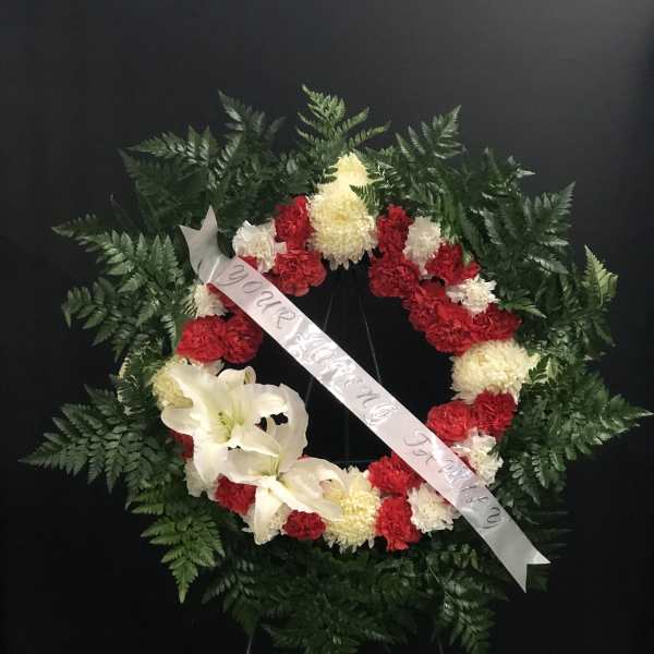 Circular funeral wreath with red and white flowers and a white ribbon