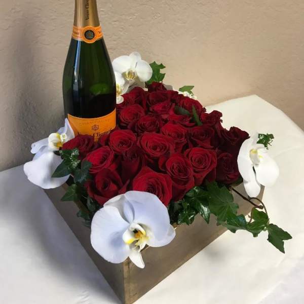 Red roses arranged with white orchids and a champagne bottle