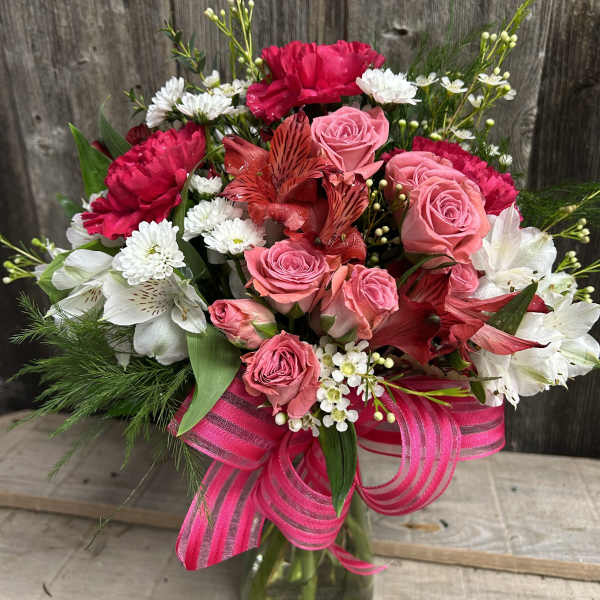Pink roses and red carnations in a glass vase with a striped ribbon