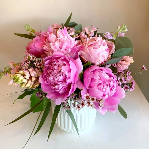 Pink peonies and small pink flowers arranged in a white vase