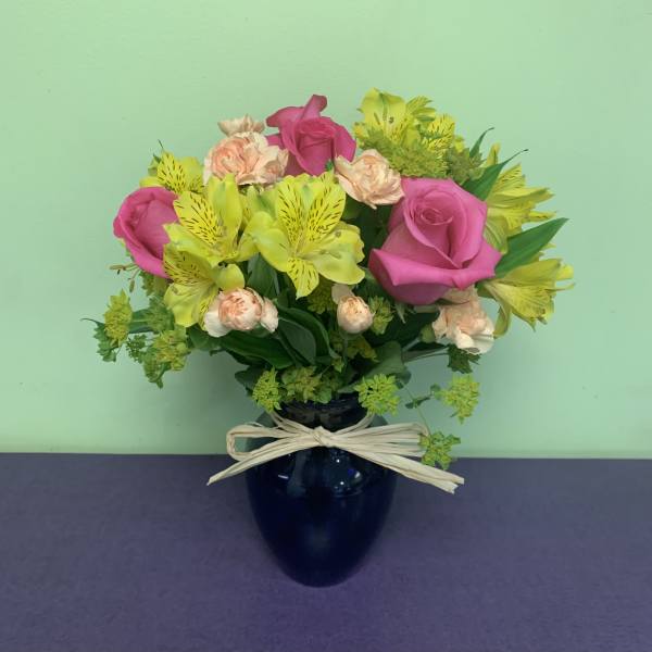 Pink roses and yellow alstroemeria in a dark vase with a bow