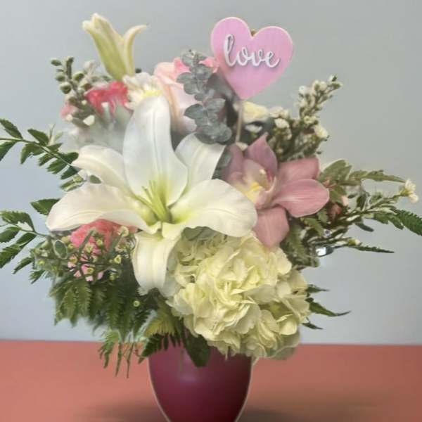 Bouquet of white lilies and pink flowers in a purple vase with a pink heart pick