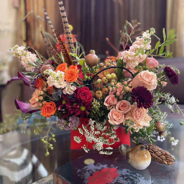 Mixed bouquet with roses, chrysanthemums, and decorative bird accents in a red container