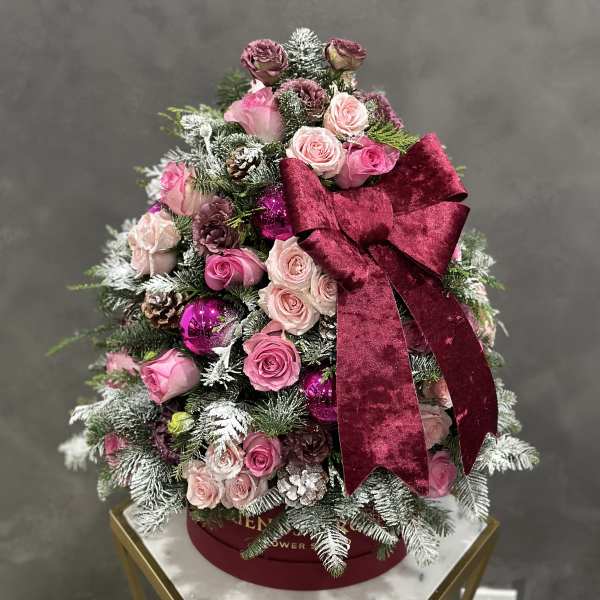Pink roses arranged like a Christmas tree with a burgundy bow and ornaments