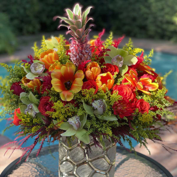 Bright mixed bouquet in a textured glass vase with red, orange, and green blooms