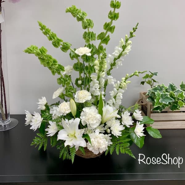 White lilies and daisies in a low basket arrangement with tall green spikes