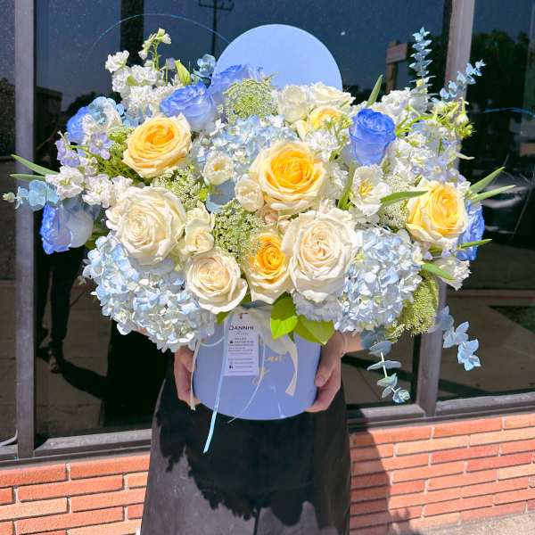Large bouquet of blue, white, and yellow roses in a round box