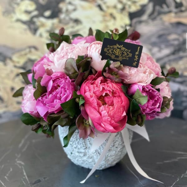 Pink peony bouquet in a textured white vase with a ribbon