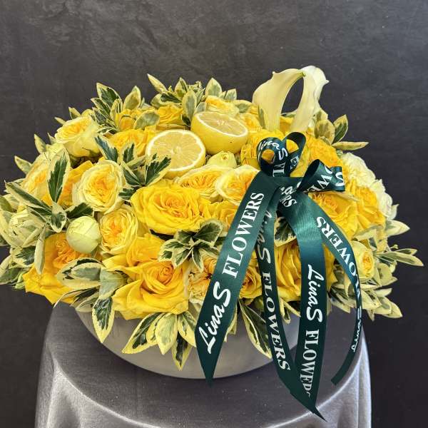 Yellow rose arrangement with lemon halves and a green ribbon in a round box