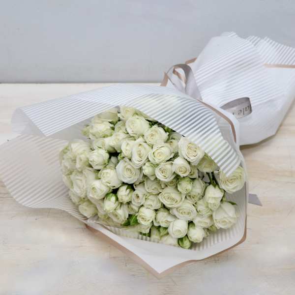 Large bouquet of white roses wrapped in striped white paper with a ribbon.