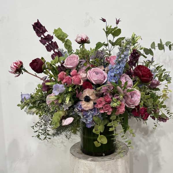 Large mixed bouquet in a dark green vase with pink, burgundy, and blue flowers