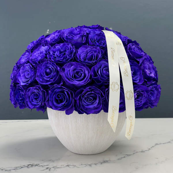 Purple rose arrangement in a white vase with a ribbon