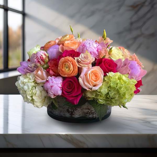 Mixed bouquet of roses, ranunculus, and hydrangeas in a low round container