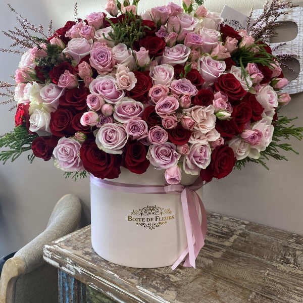 Large pink and red rose arrangement in a round hat box with ribbon