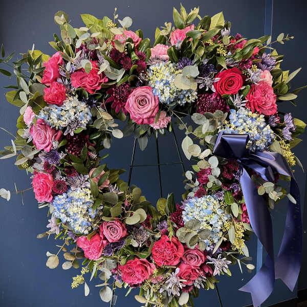 Heart-shaped floral wreath with pink, purple, and blue flowers on a dark stand