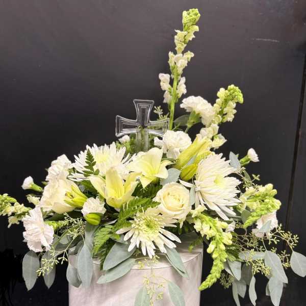 White floral arrangement with a clear cross pick in a pale container