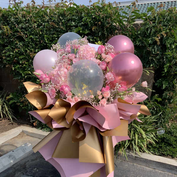 Pink floral arrangement with balloons and metallic wrapping on a stand