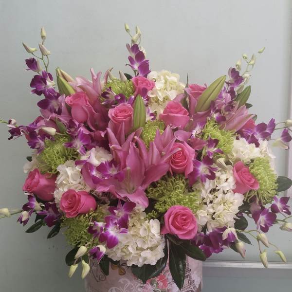 Pink roses and lilies arranged with purple orchids in a decorative box