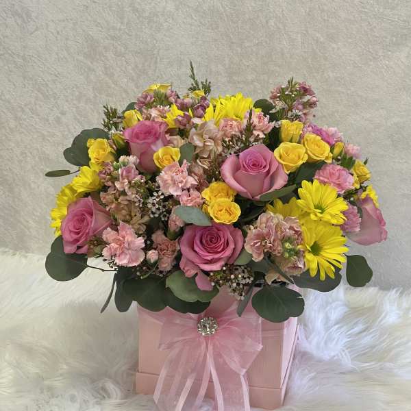 Pink and yellow mixed flower arrangement in a pink gift box with ribbon