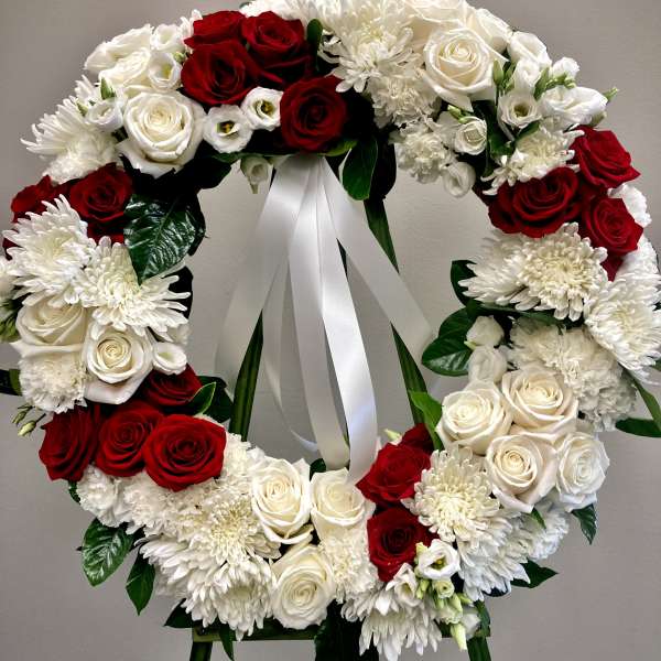 Circular wreath of red and white flowers on an easel with a white ribbon